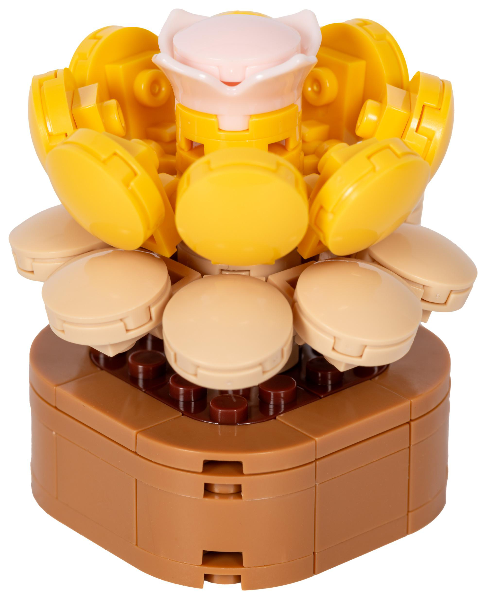 Eine Lego-Kreation, die einer Blume mit gelben Blütenblättern, hellbraunen Keksen und einem braunen Sockel auf weißem Grund ähnelt.