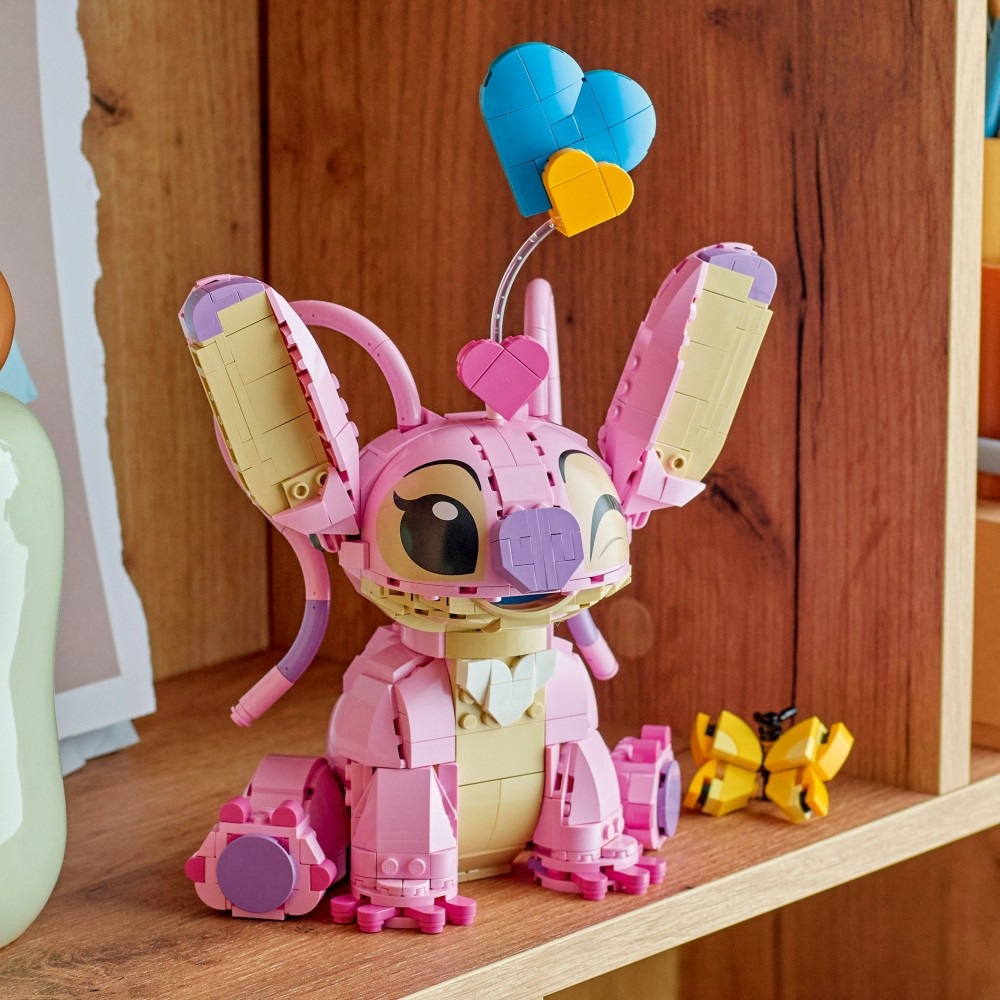 Różowa figurka Lego Angel z balonami w kształcie serca. Żółty motyl Lego po prawej. Drewniana półka w tle.