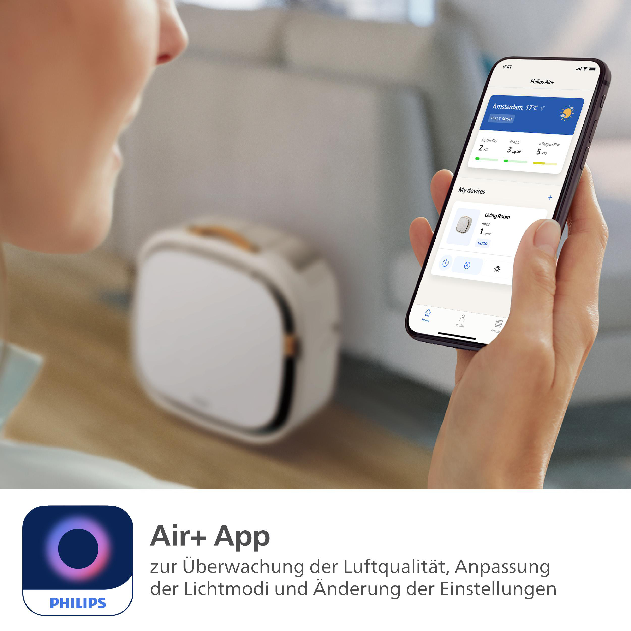 Person hält Telefon mit Luftqualitätsdaten. Weißer Luftreiniger und Air+ App-Logo sind sichtbar.