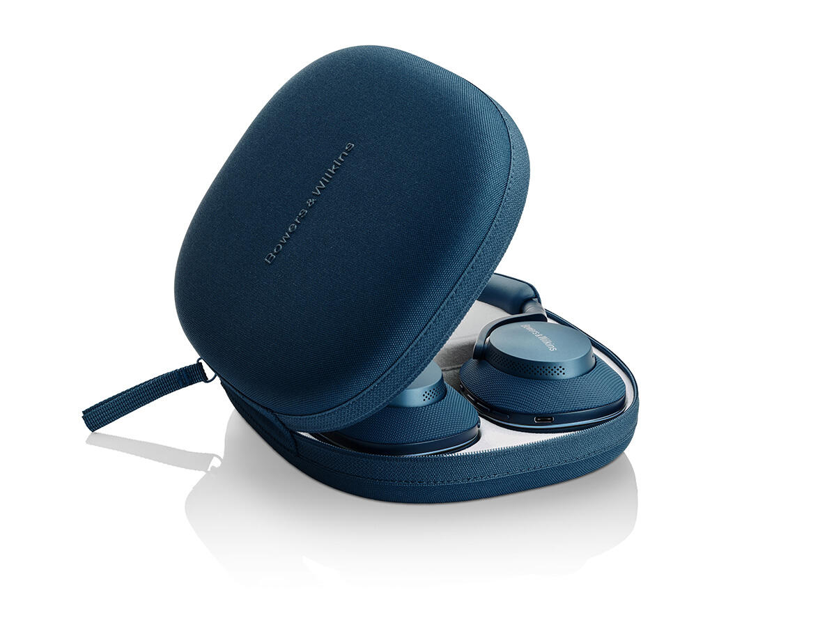 Kék fejhallgató egy nyitott tokban. A tokon a 'Bowers & Wilkins' felirat látható. A fejhallgatók fehér felületen helyezkednek el.