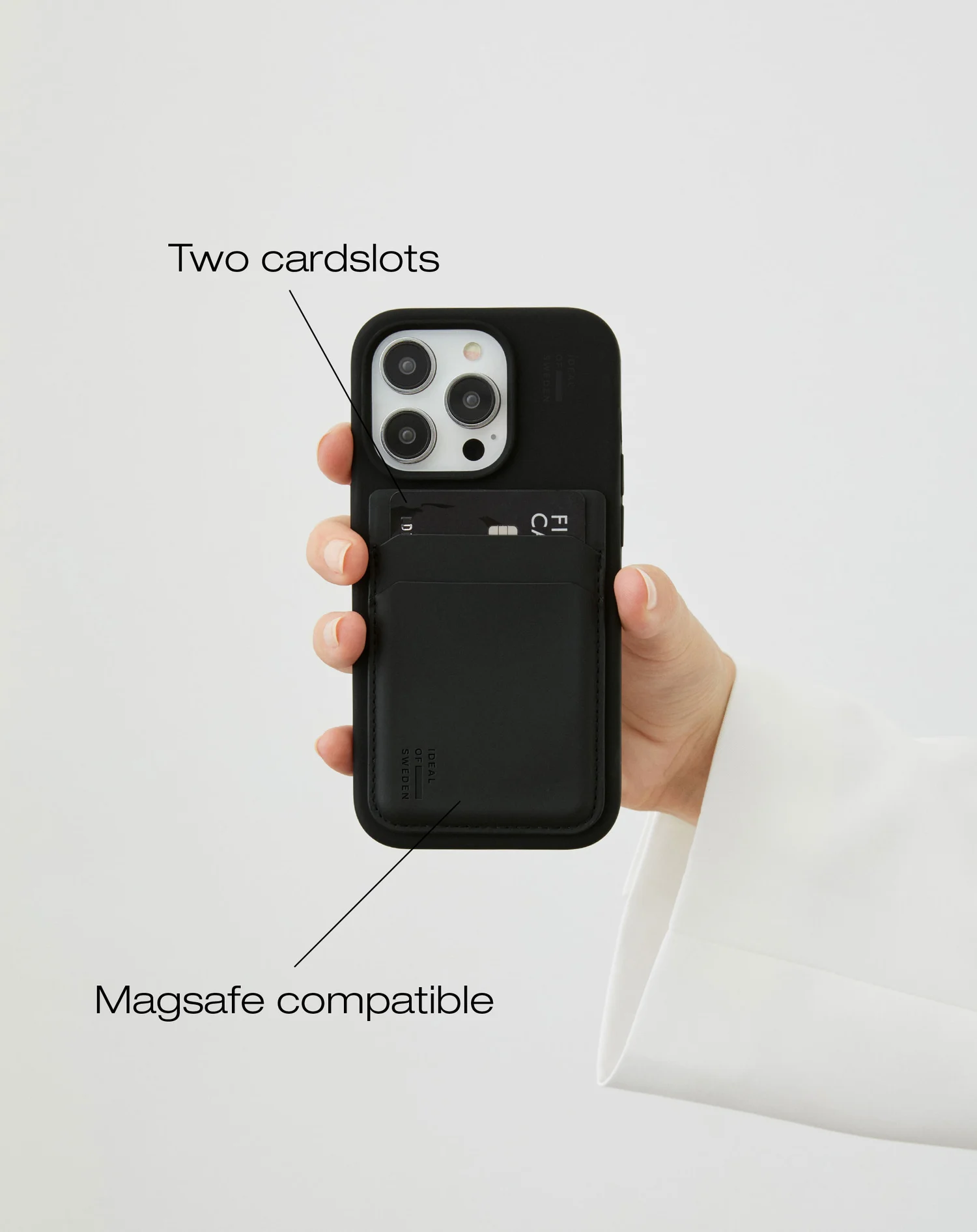 Egy kéz egy fekete telefontokot tart, benne kártyanyílásokkal. A tok fehér háttér előtt van. Magsafe kompatibilis.