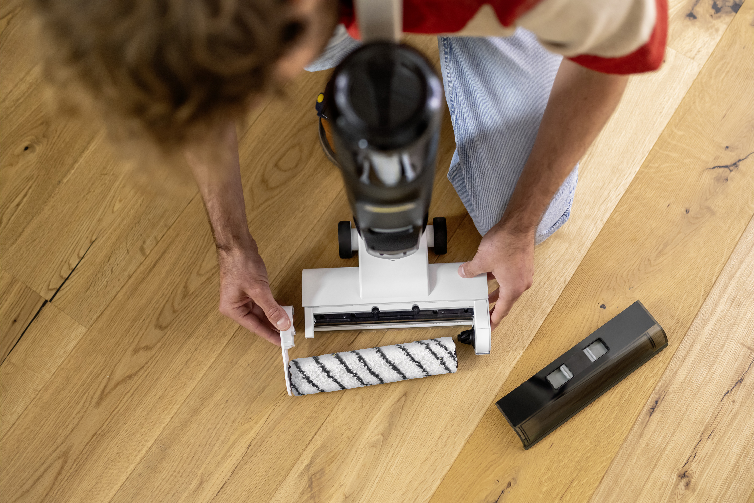 Osoba montująca odkurzacz na drewnianej podłodze. Wałek odkurzacza jest wkładany.