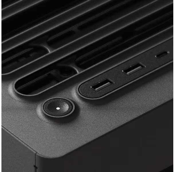 Nahaufnahme einer dunklen Computerkomponente mit Ein-/Aus-Taste, USB-Anschlüssen und Lüftungsschlitzen. Die Oberfläche ist strukturiert.