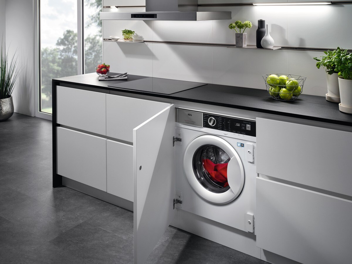 Cocina moderna con lavadora. Armarios blancos, encimera negra y ventana al fondo.