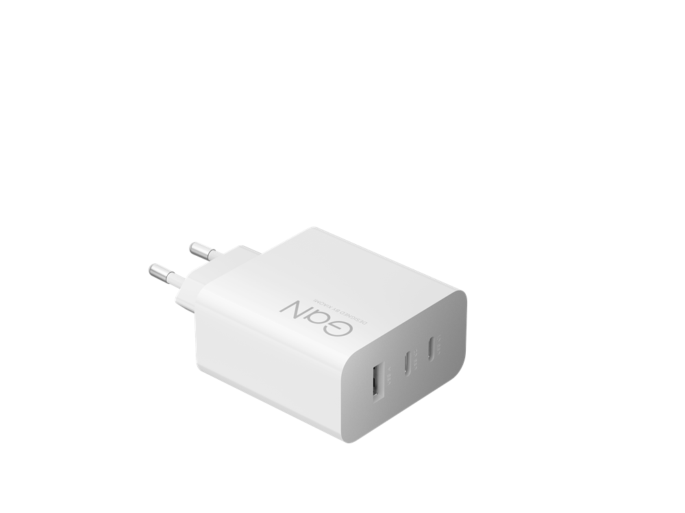 Egy fehér GAN töltő, három USB-porttal és két fémcsatlakozóval. A töltő fekete háttéren van. A 'GAN' felirat látható.
