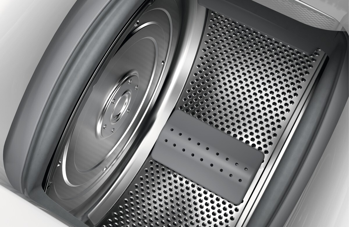 Interior de una lavadora. Se ve un tambor metálico, con un panel de acero inoxidable perforado. También se ve una pieza de plástico gris.