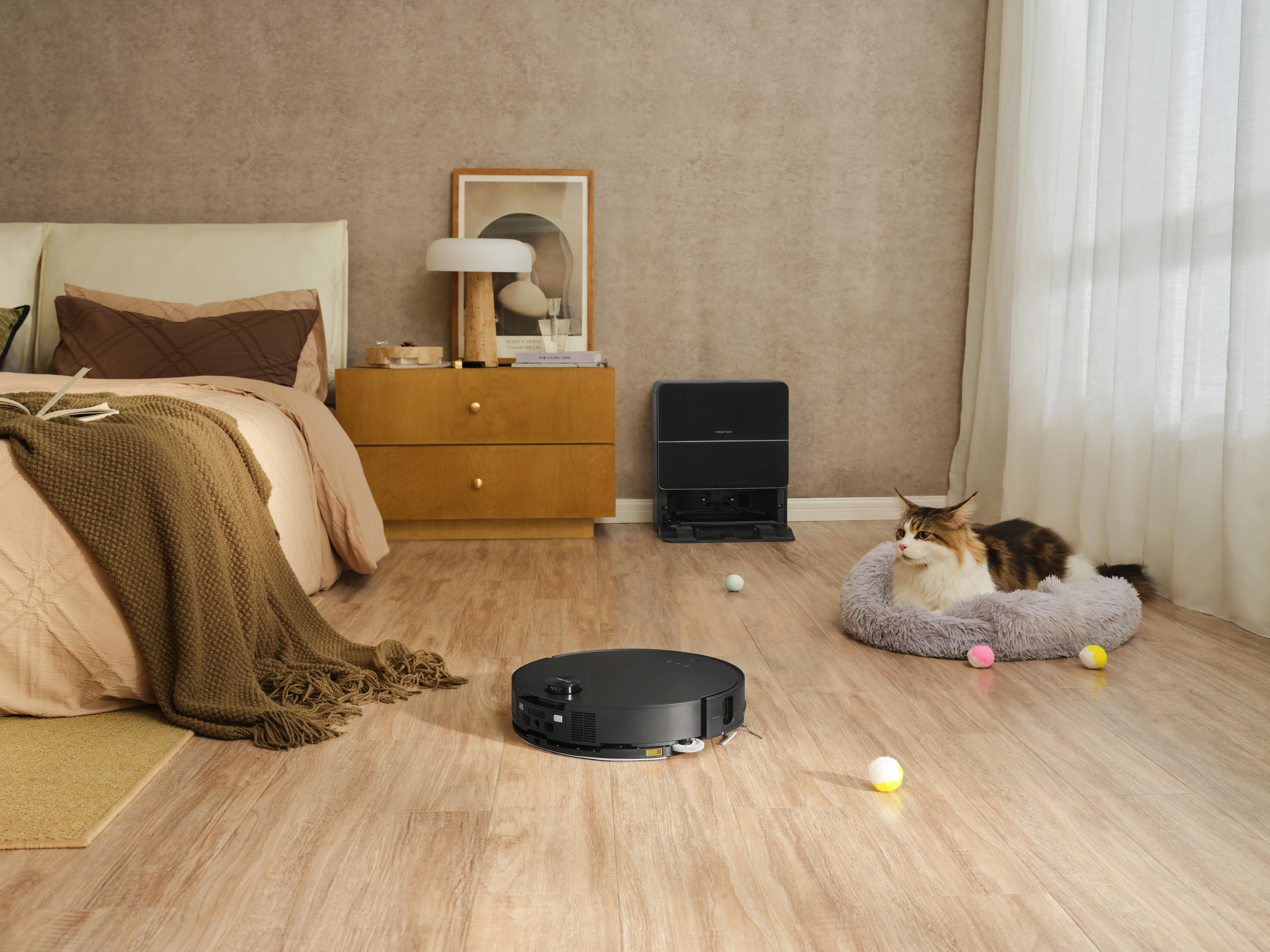 Ein Schlafzimmer mit Bett, Staubsaugerroboter, Katze im Bett und Ladestation.