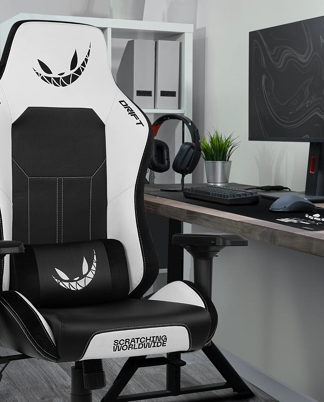 Silla gaming con diseño blanco y negro. Escritorio con ordenador, auriculares y teclado al fondo. Estantería blanca.