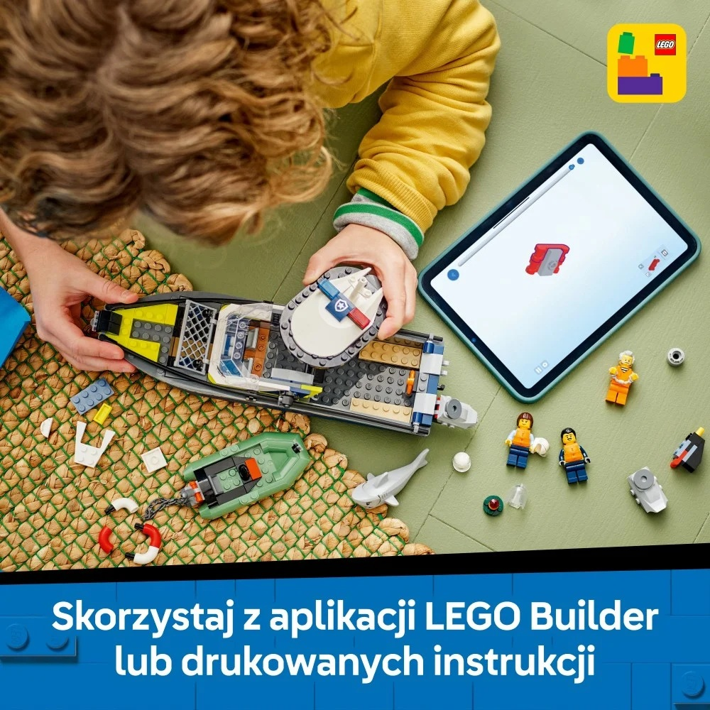 Dziecko składa łódź Lego z instrukcjami na tablecie. Figurki Lego i rekin na zielonej powierzchni.