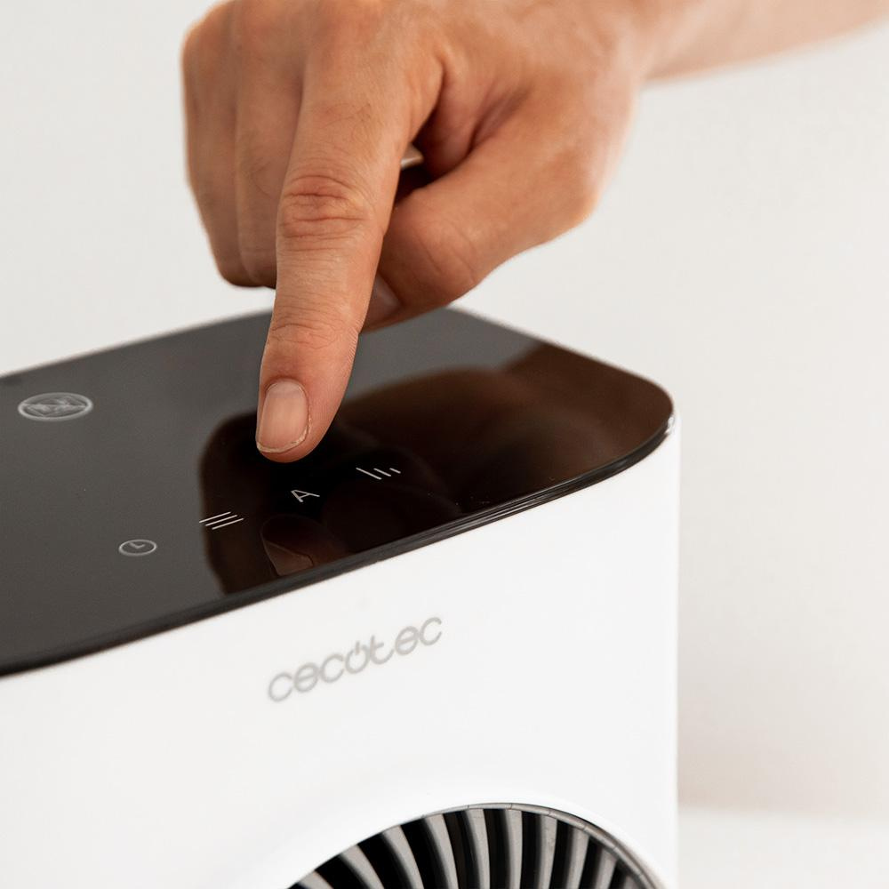 Una mano presiona un botón en un electrodoméstico blanco. El aparato tiene una parte superior negra con símbolos y la marca 'cecotec'.