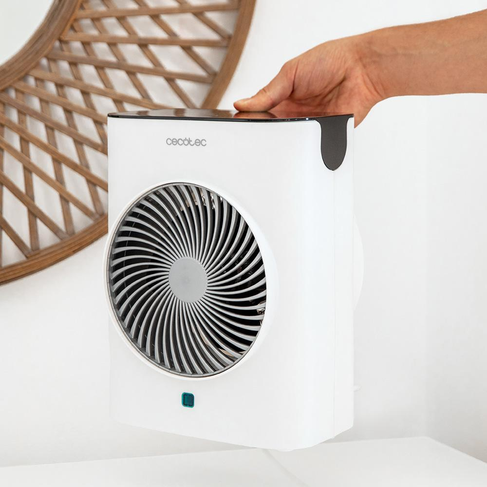 Un purificador de aire blanco con ventilador circular. Una mano sujeta la parte superior. Una pieza decorativa de madera en el fondo.