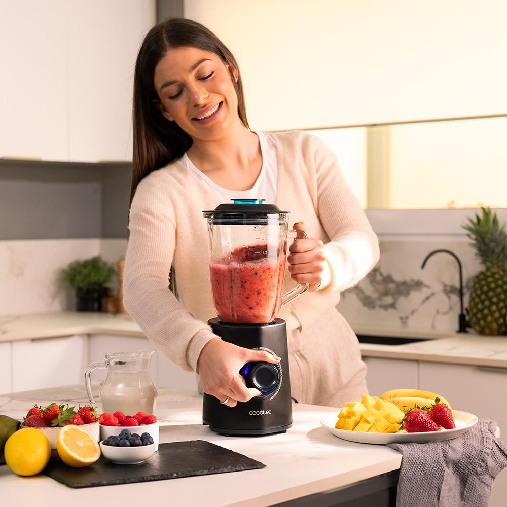 Mujer haciendo un batido. Licuadora con mezcla roja. Frutas como fresas, mangos, limones en la encimera.