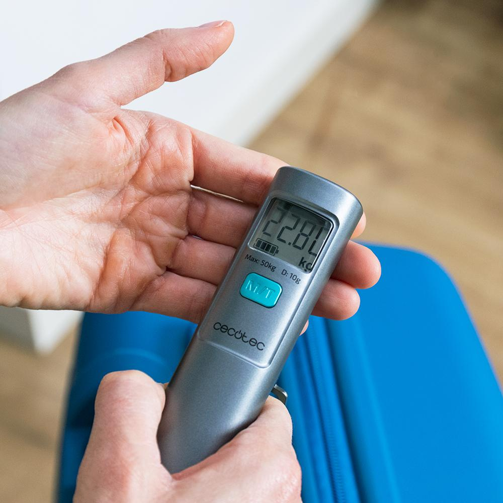 Una persona sostiene una báscula digital para equipaje. La báscula muestra 22,80 kg. Una maleta azul está en el fondo.