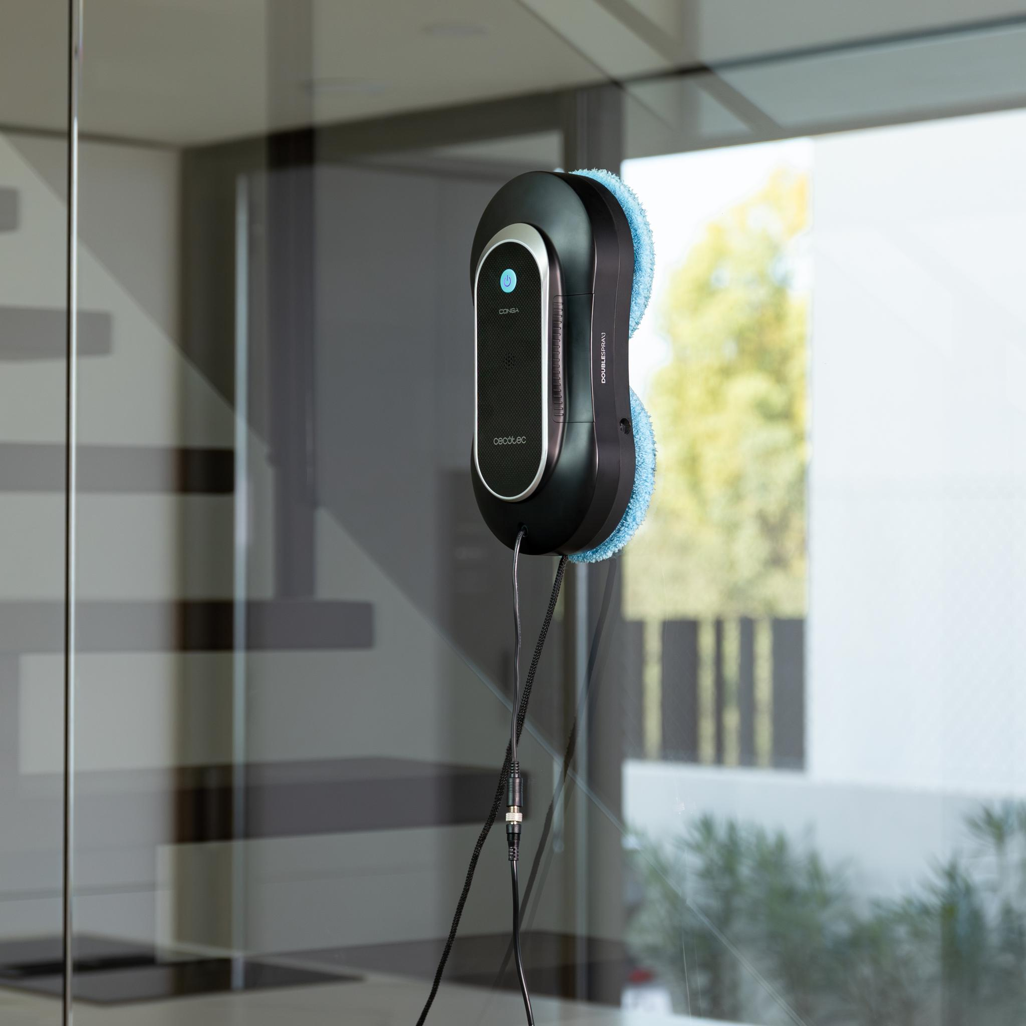 Un robot limpiacristales negro y azul está adherido a la ventana. Tiene un cable de alimentación.
