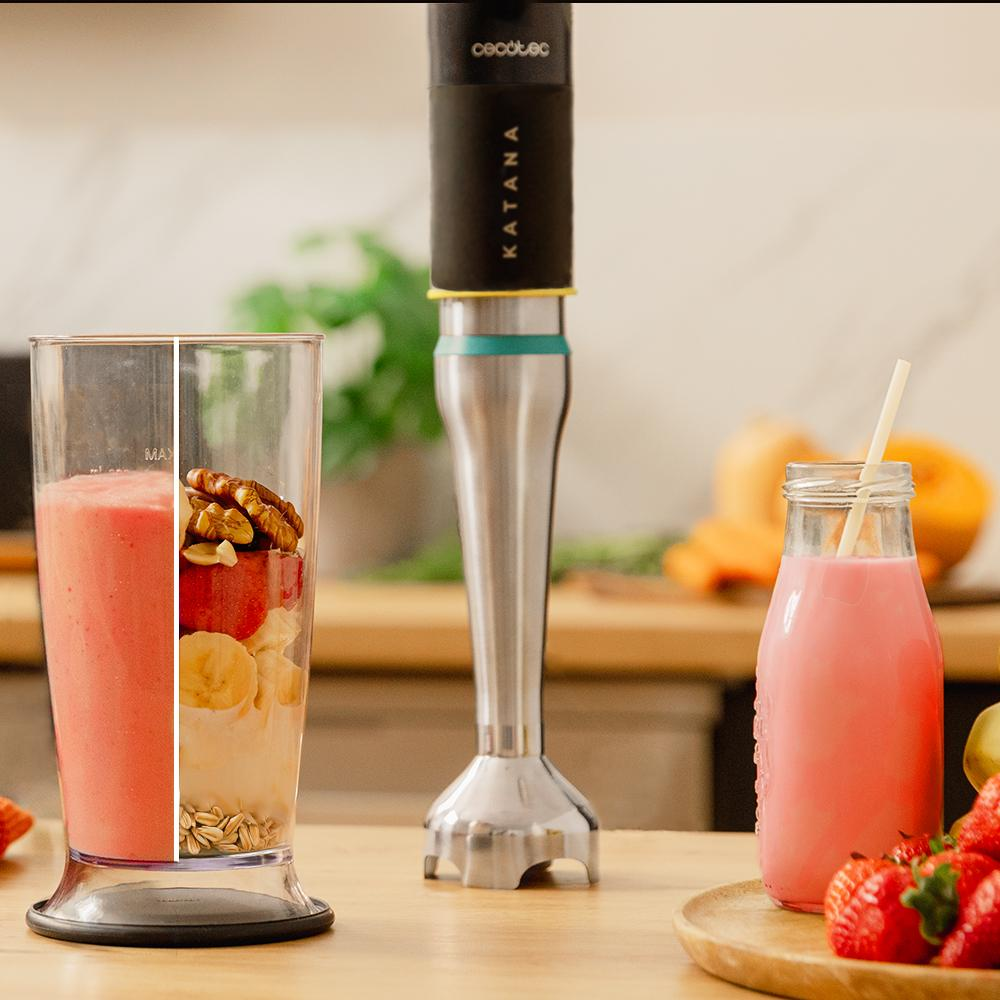 Una licuadora junto a un vaso con fruta y una botella de batido rosa, con fresas. El fondo muestra una cocina.