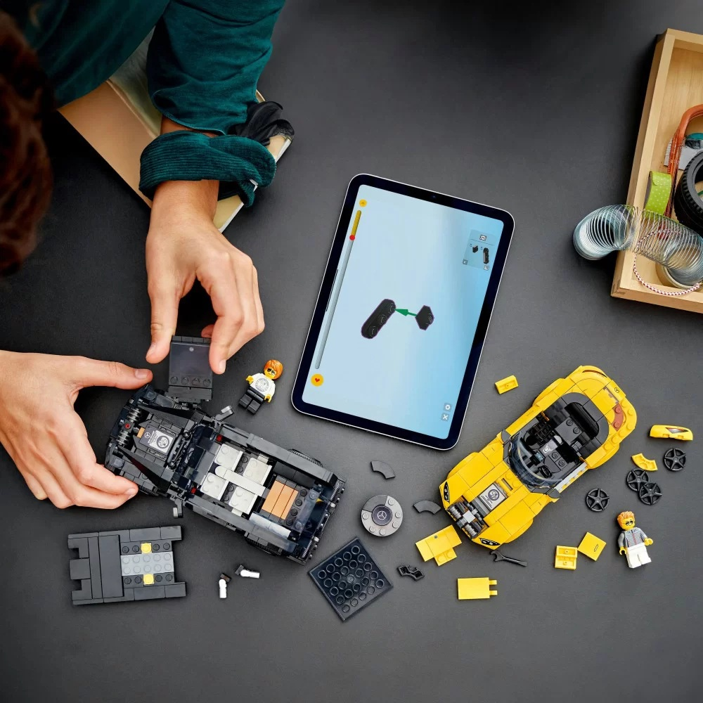 Ręce składają czarny samochód Lego. Żółty samochód Lego i tablet z instrukcjami są w pobliżu. Inne elementy Lego są rozrzucone.