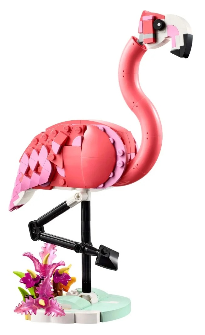 Flaming z klocków Lego, wykonany z różowych i białych klocków, stojący na zielonej podstawie z kwiatami. Jego szyja jest wygięta.
