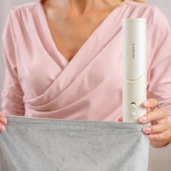 Kobieta w różowej bluzce trzyma białe urządzenie nad szarą tkaniną. Urządzenie ma przyciski i napis 'MDM'.