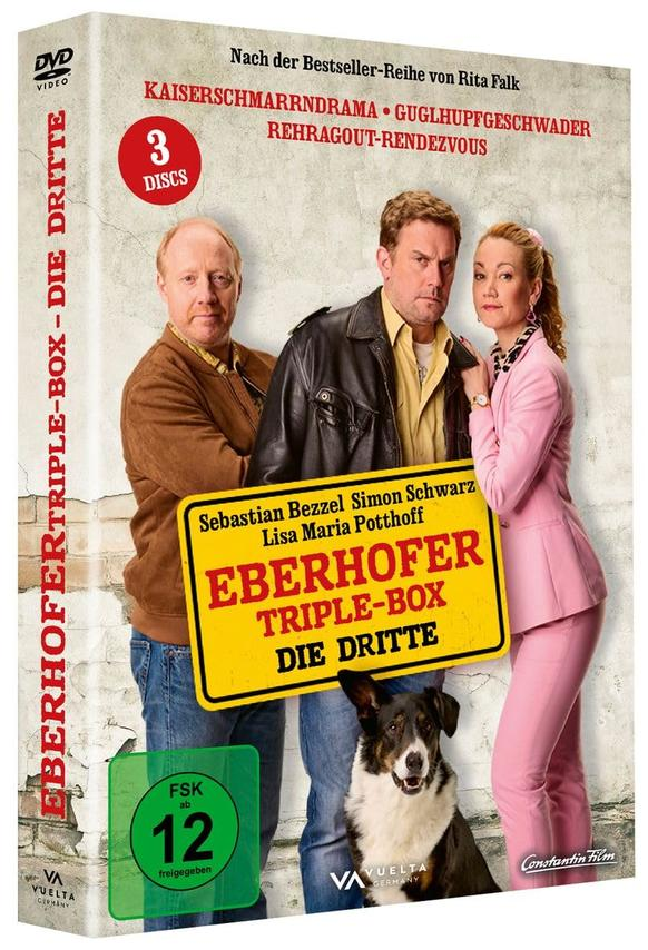 DVD-Cover. Drei Personen und ein Hund stehen vor einem Filmtitel. Der Titel lautet Eberhofer Triple-Box Die Dritte.