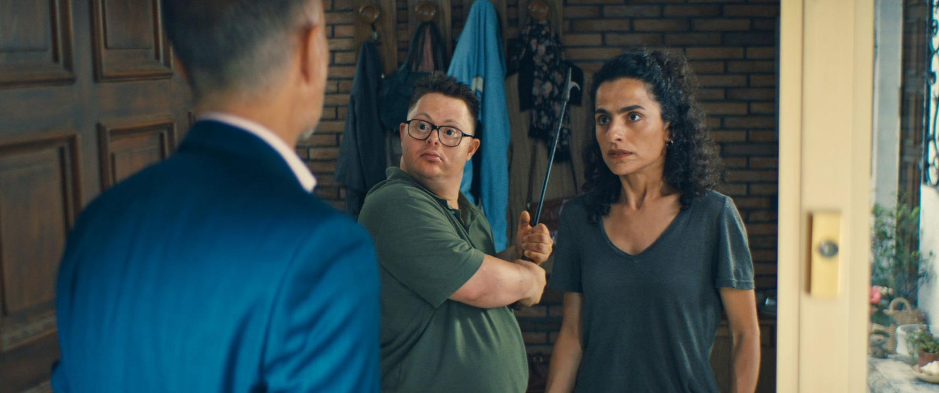 Drei Personen in einer Tür. Ein Mann im blauen Anzug ist abgewandt. Ein Mann mit Brille und eine Frau halten einen Stock.