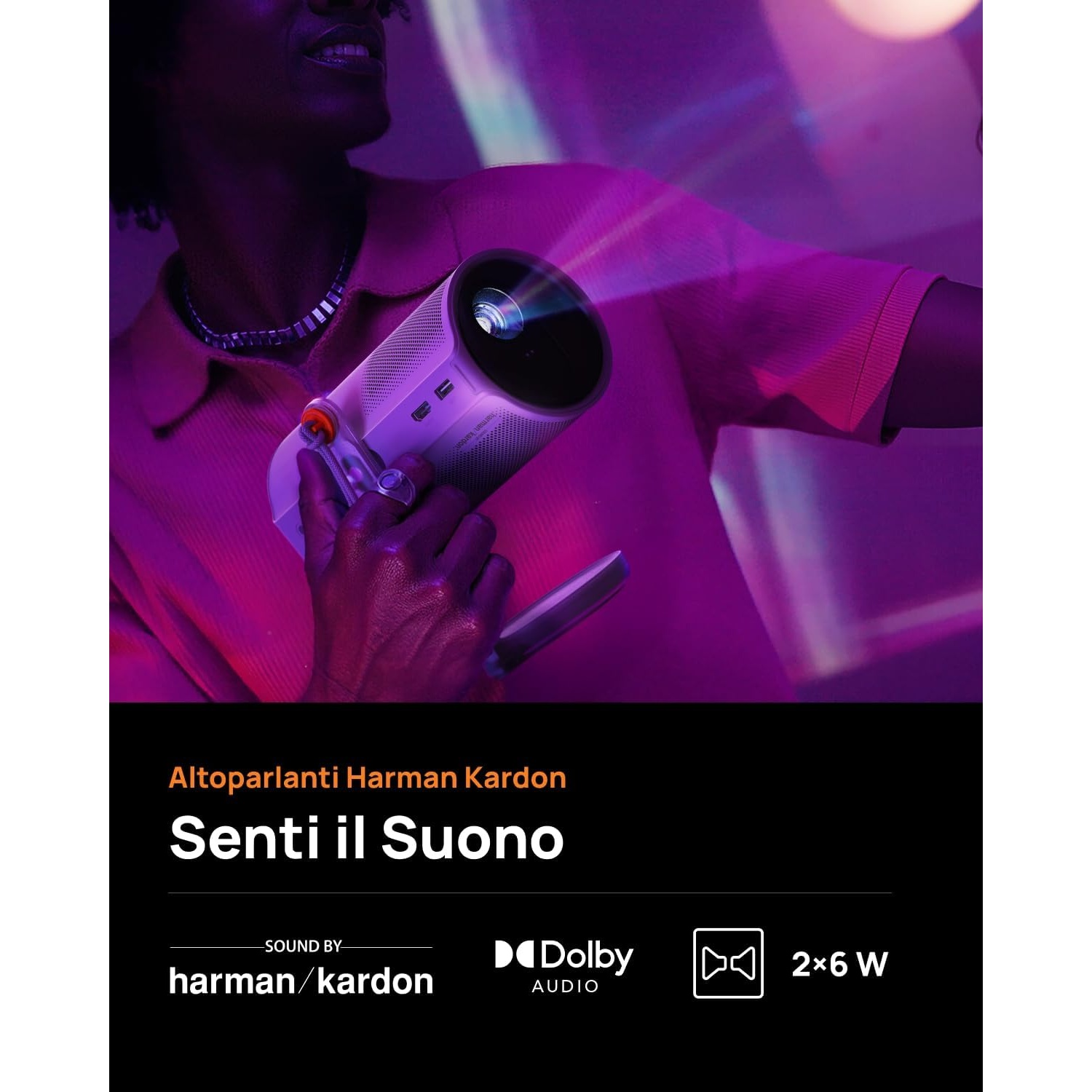 Una persona tiene in mano un proiettore. L'immagine è viola e presenta il testo 'Senti il Suono' e 'harman/kardon Dolby Audio'.