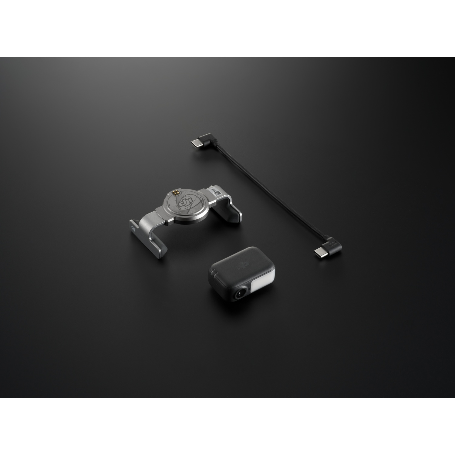 A product setup. Includes a silver bracket, a small camera, and a black cable with connectors, all on a black surface.