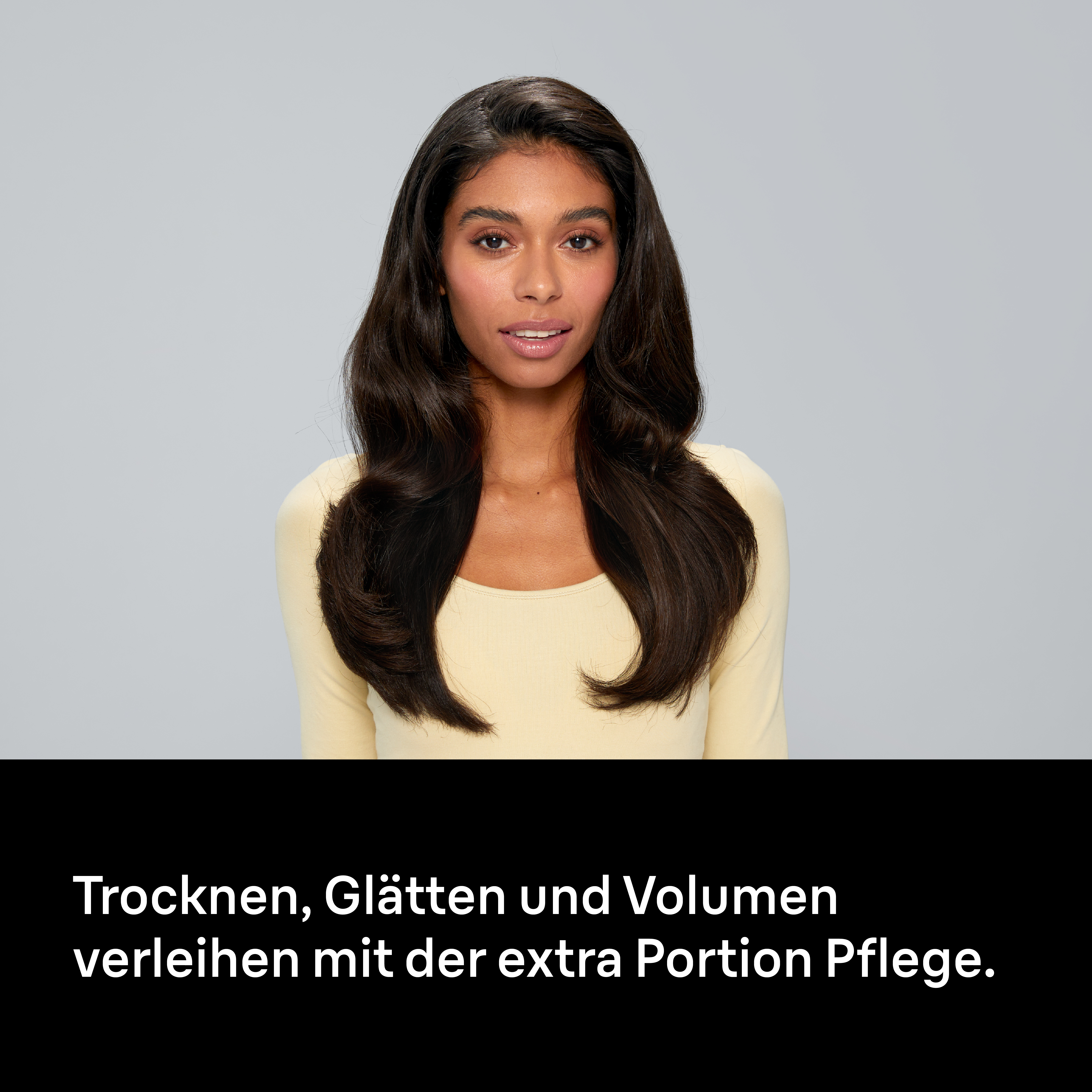 Eine Frau mit langen dunklen Haaren trägt ein gelbes Oberteil. Text unten: Trocknen, Glätten und Volumen.