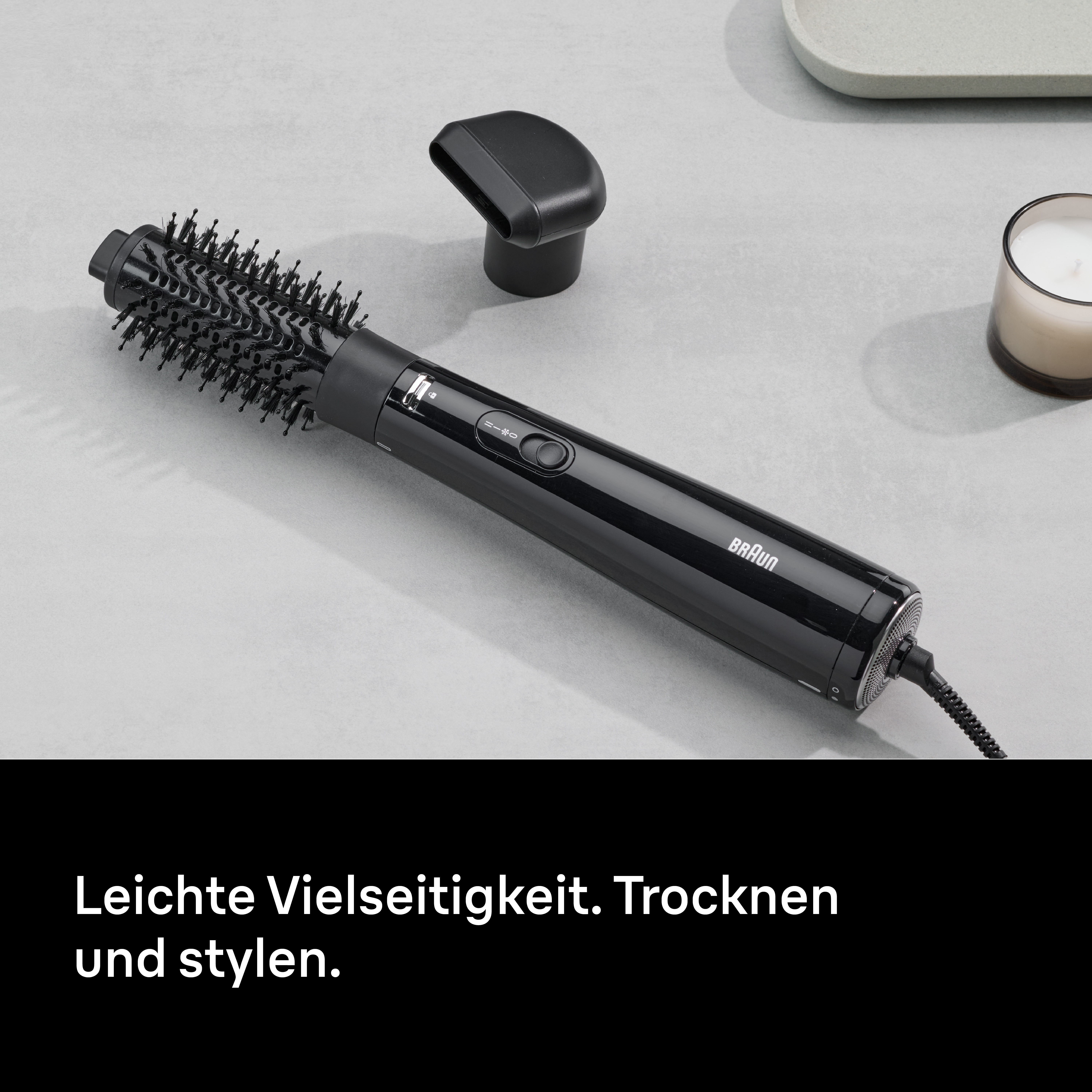 Schwarzer Braun Haarstyler mit Aufsätzen auf grauer Oberfläche. Eine Kerze und eine Ablage sind auch sichtbar.