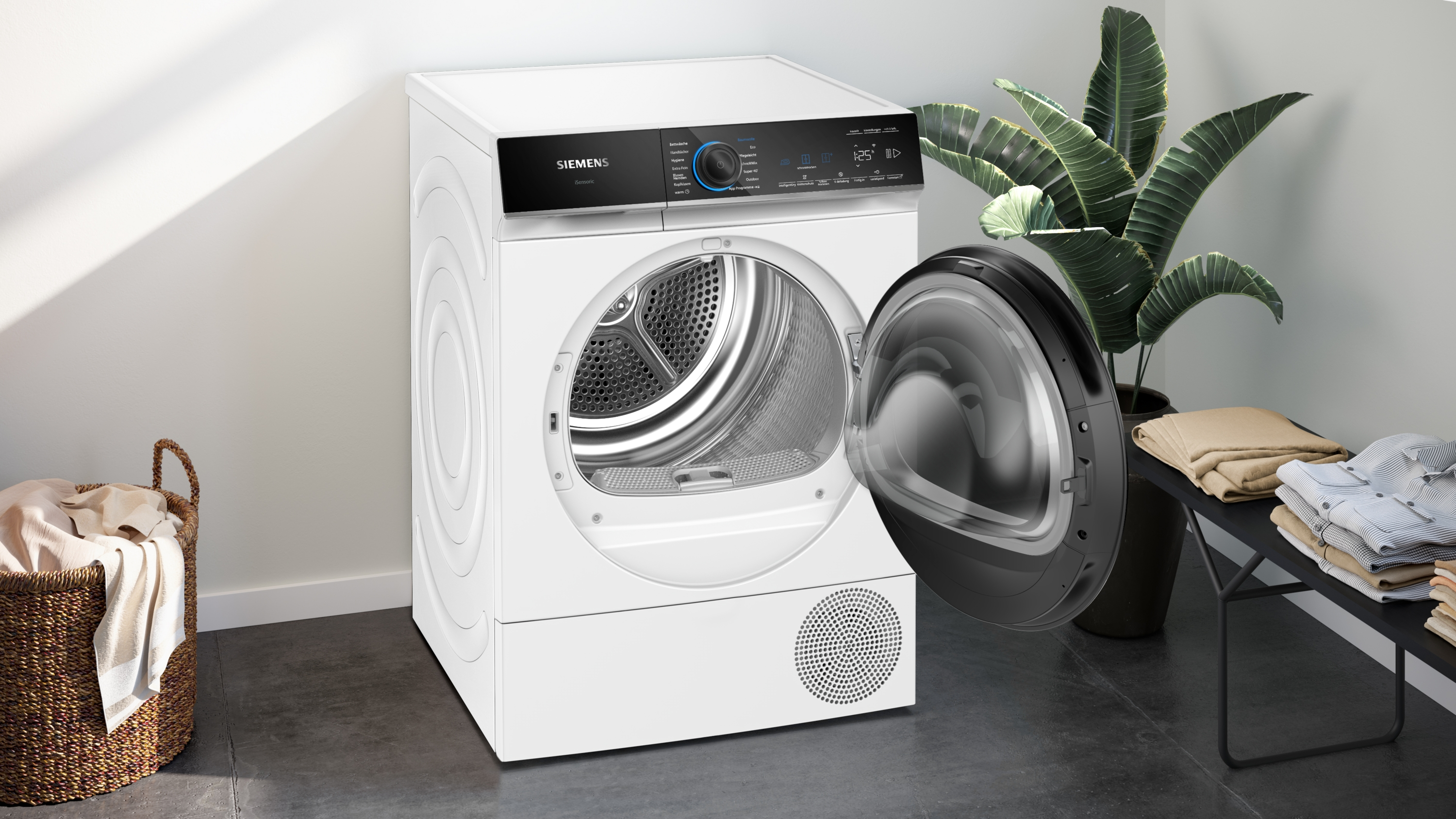 Ein weißer Siemens-Trockner mit offener Tür. Ein Wäschekorb und eine Pflanze befinden sich an den Seiten. Kleidung liegt auf einer Bank.