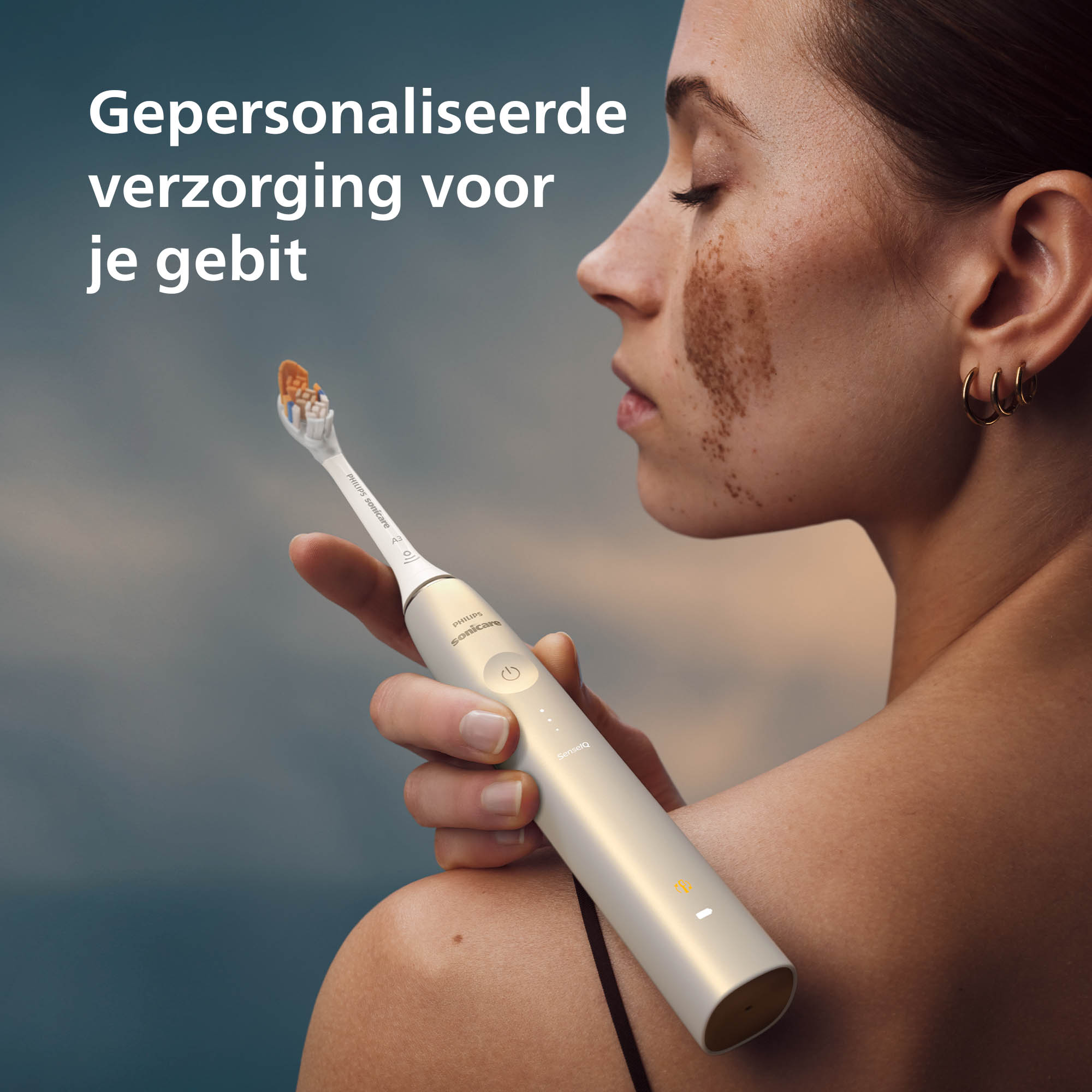Woman holding a toothbrush. The toothbrush is white and gold. The background is blurred.