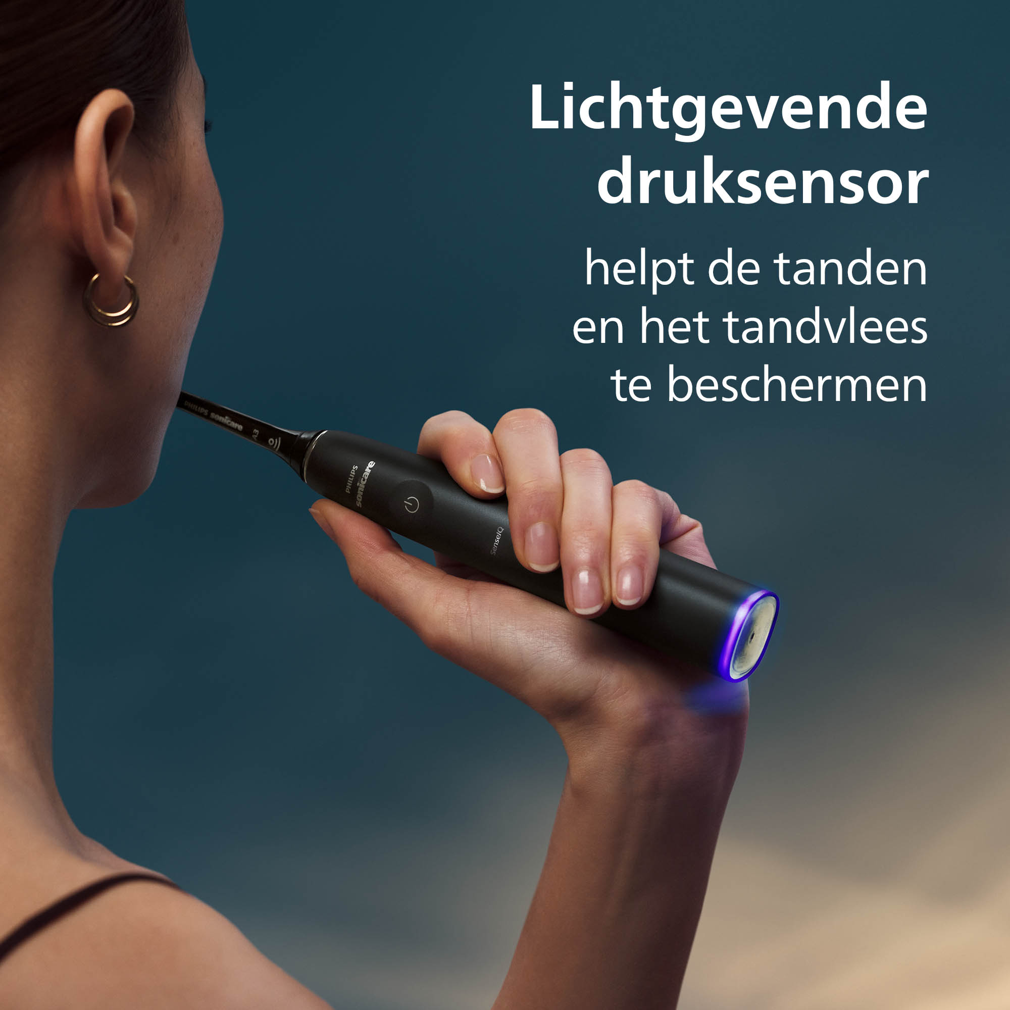 Een vrouw houdt een zwarte elektrische tandenborstel met blauw licht vast. De tekst zegt 'druksensor beschermt tanden'.
