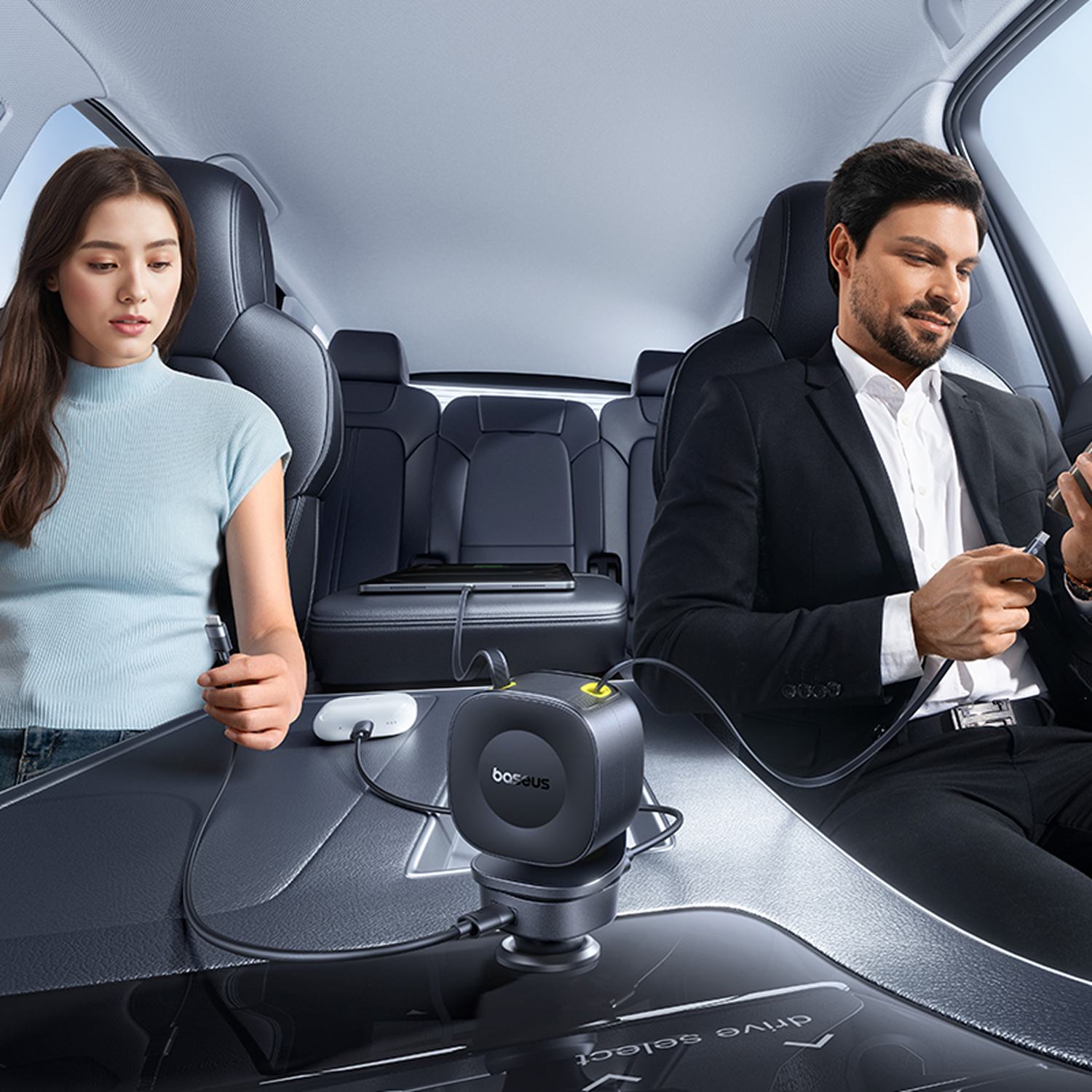 Dentro de un coche, una mujer y un hombre usan sus teléfonos. Un cargador negro está entre ellos.