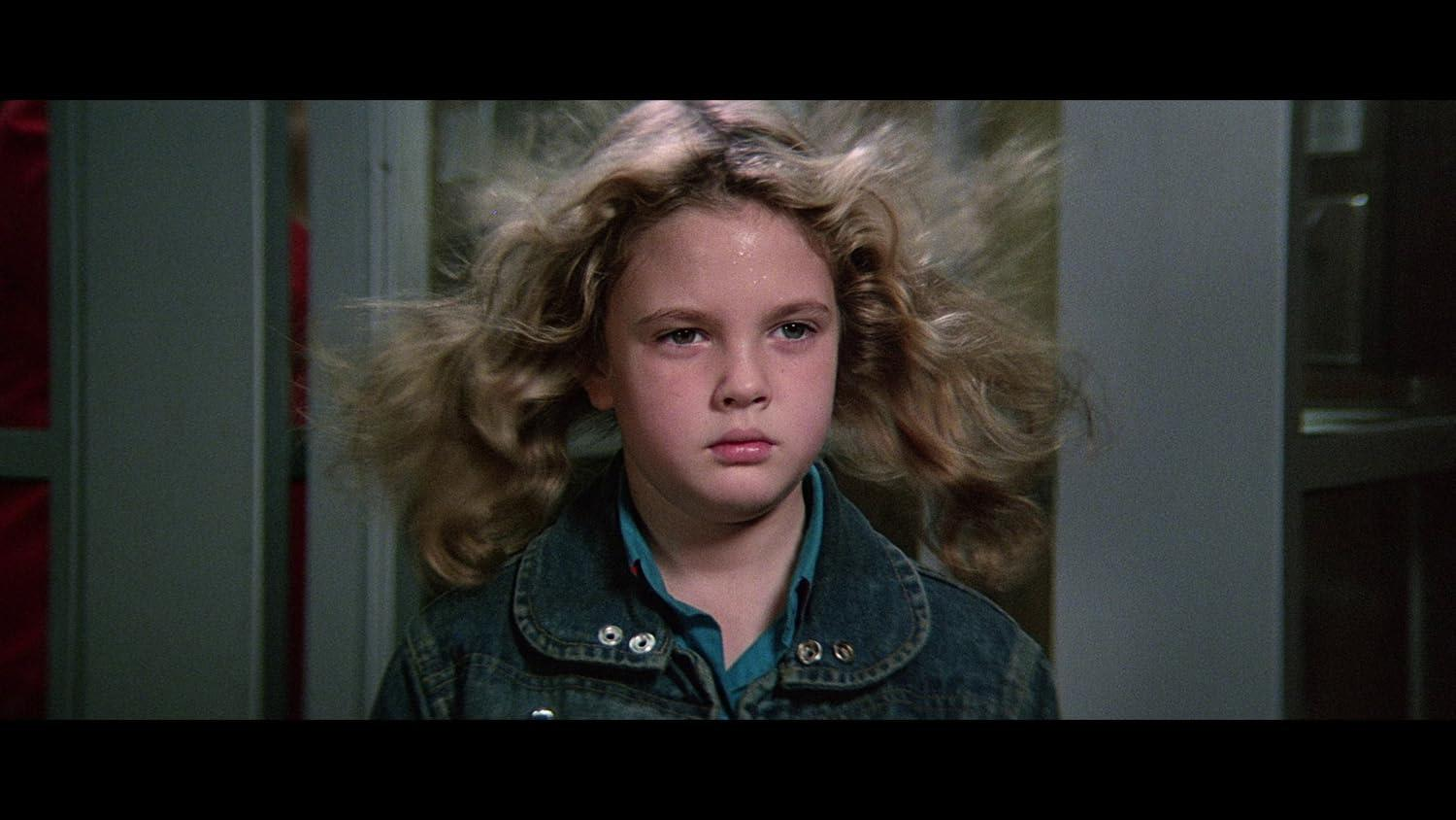 Ein junges Mädchen mit blonden Haaren und einer Jeansjacke blickt nach vorne. Ihr Haar ist leicht zerzaust. Der Hintergrund ist unscharf.