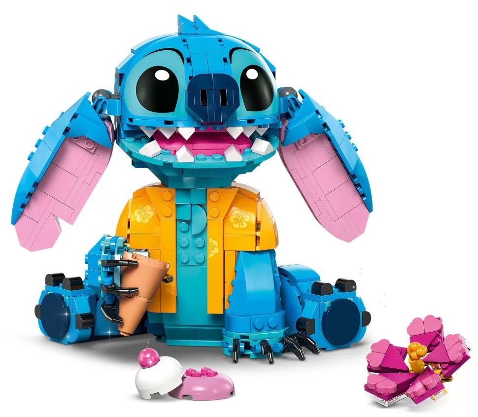 Figurka Lego Stitch, z żółtą koszulą, trzymająca kubek. Na podłodze ciasto i kwiat z klocków Lego.