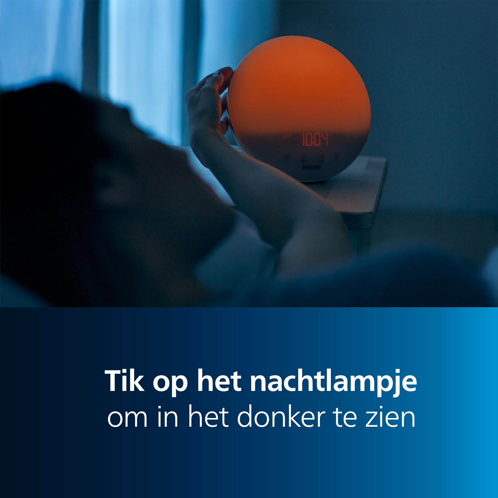 A person in bed reaches for a round orange alarm clock on a nightstand. The time is 10:04.