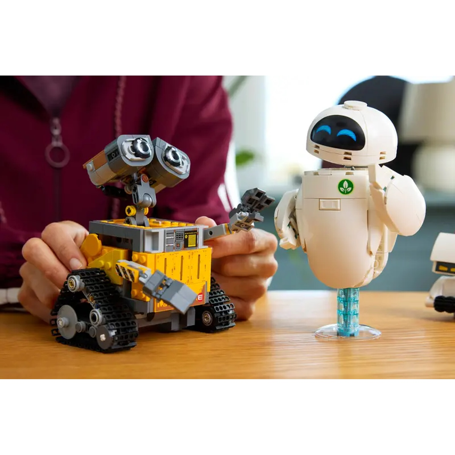 Deux robots Lego, Wall-E et Eve, sur une table en bois. Les mains d'une personne sont près de Wall-E.