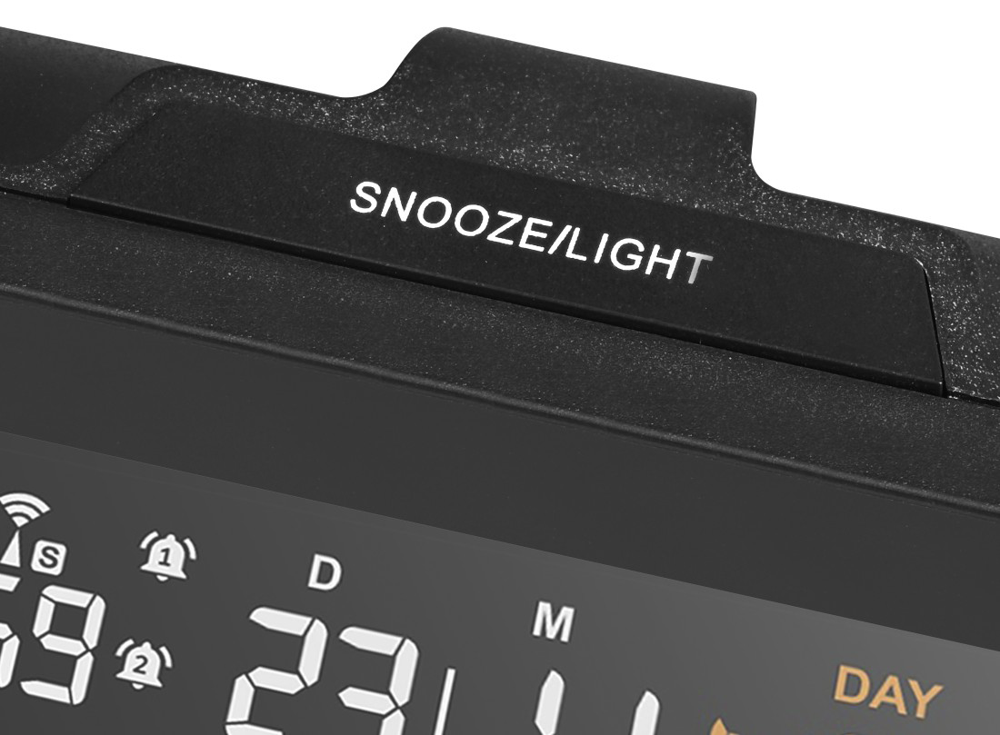 Fekete ébresztőóra részlete a 'SNOOZE/LIGHT' gombbal, időt és dátumot mutató kijelzővel.