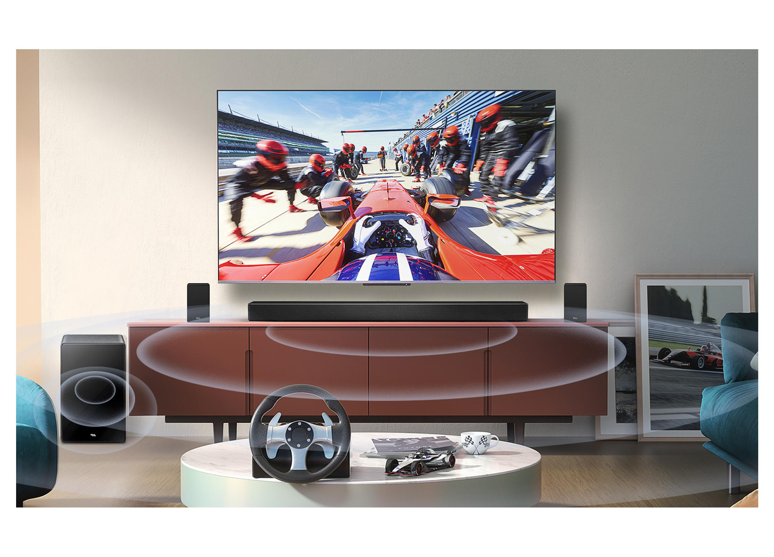 Wohnzimmer-Setup mit TV, das ein Rennen zeigt. Lautsprecher, Soundbar und Rennlenkrad auf dem Tisch.