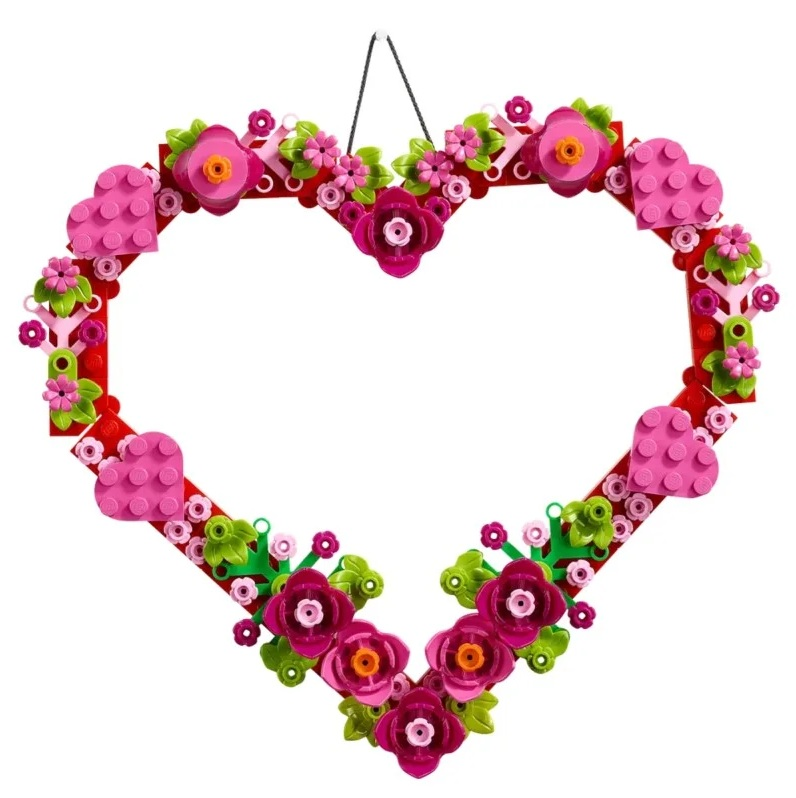 Wieniec w kształcie serca z klocków Lego, ozdobiony różowymi i fioletowymi kwiatami oraz zielonymi liśćmi. Wiszący na białym tle.