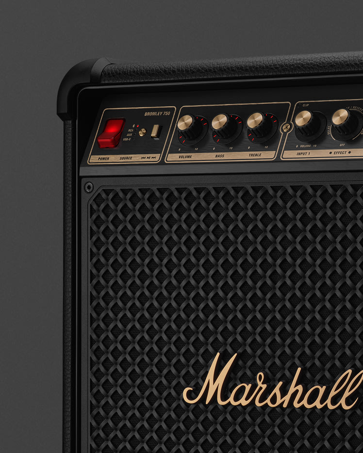 Primer plano de un amplificador Marshall negro con detalles dorados. Se ven perillas, interruptores y el nombre de la marca.