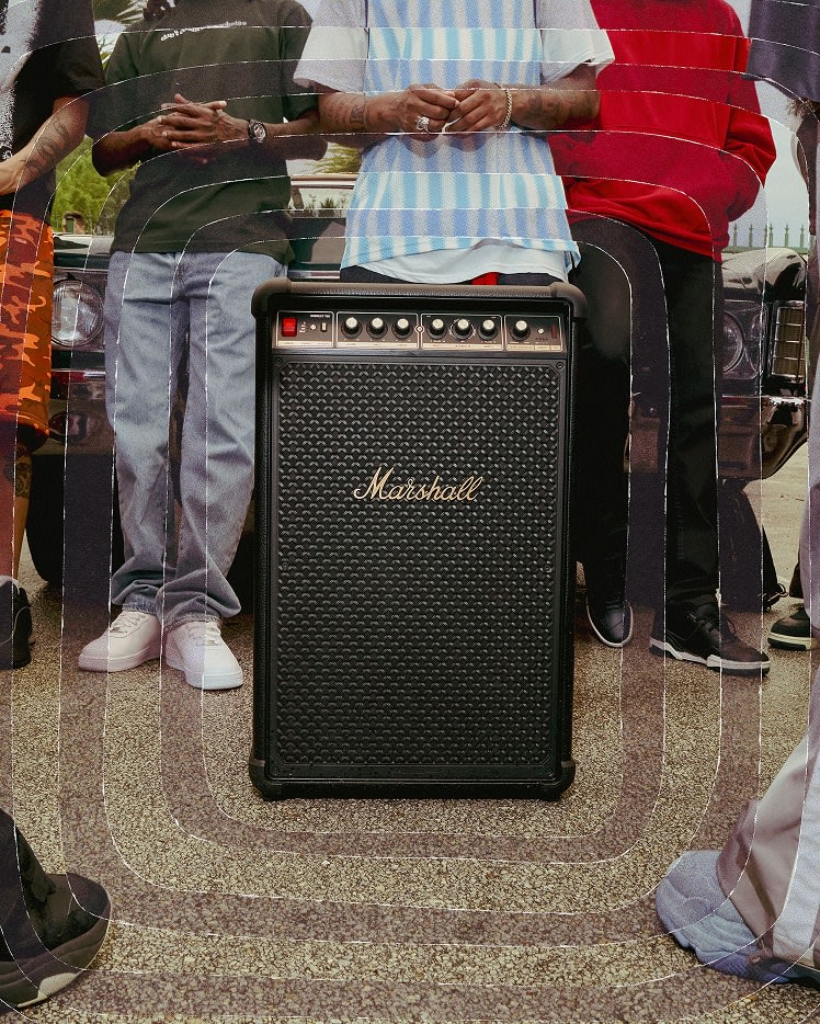 Un amplificador Marshall negro está frente a personas. La gente está de pie. El amplificador es el punto focal de la imagen.