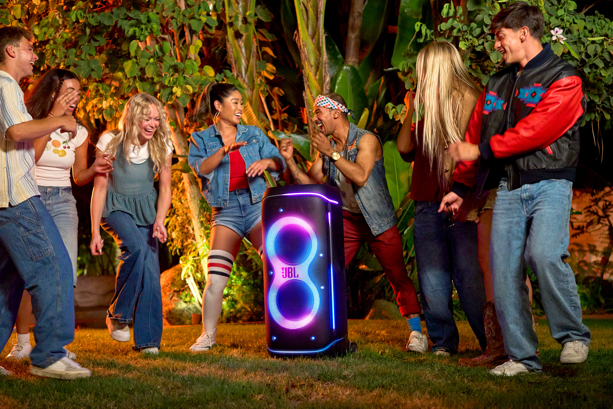 Groupe de jeunes dansant près d'une enceinte JBL la nuit. L'enceinte a une lumière vive et les gens sourient.