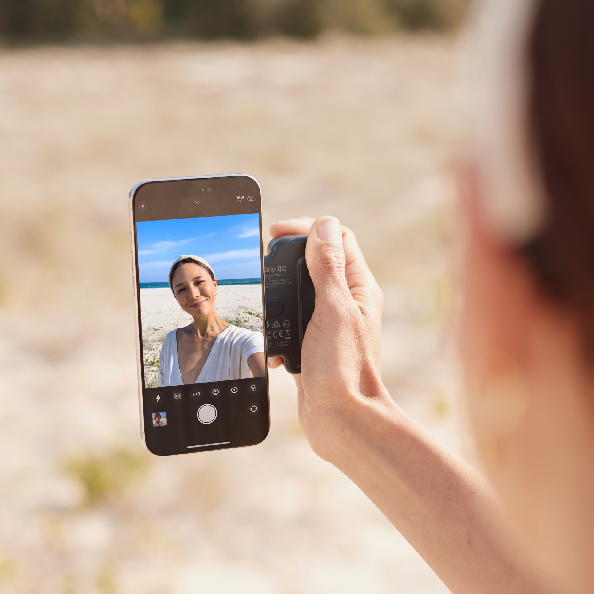 Una persona che scatta un selfie in spiaggia. Il telefono mostra la persona nell'inquadratura, che tiene un bastone per selfie.