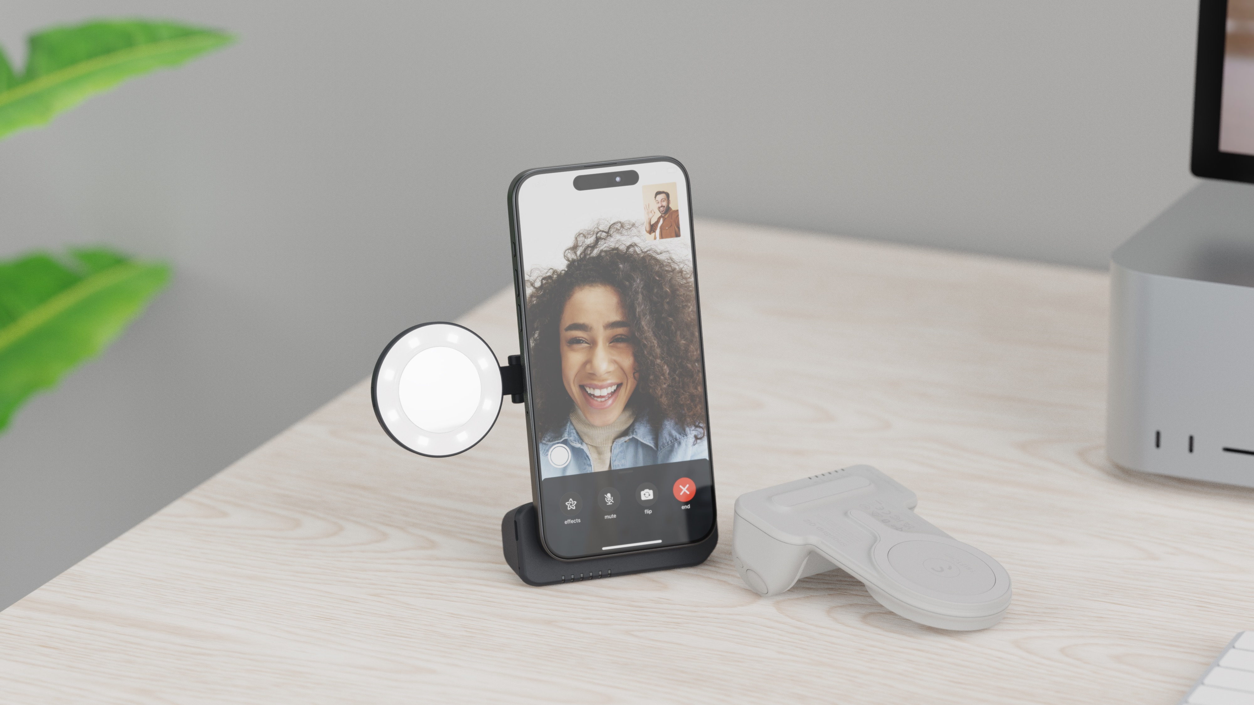 Un telefono su un supporto mostra una videochiamata. Una luce ad anello e un telecomando sono vicini. Una donna sorride sullo schermo.