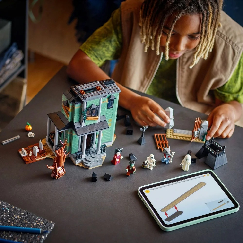 Dziecko składa nawiedzony dom z klocków Lego. Scena obejmuje figurki Lego, dynię, tablet z instrukcjami i dom.