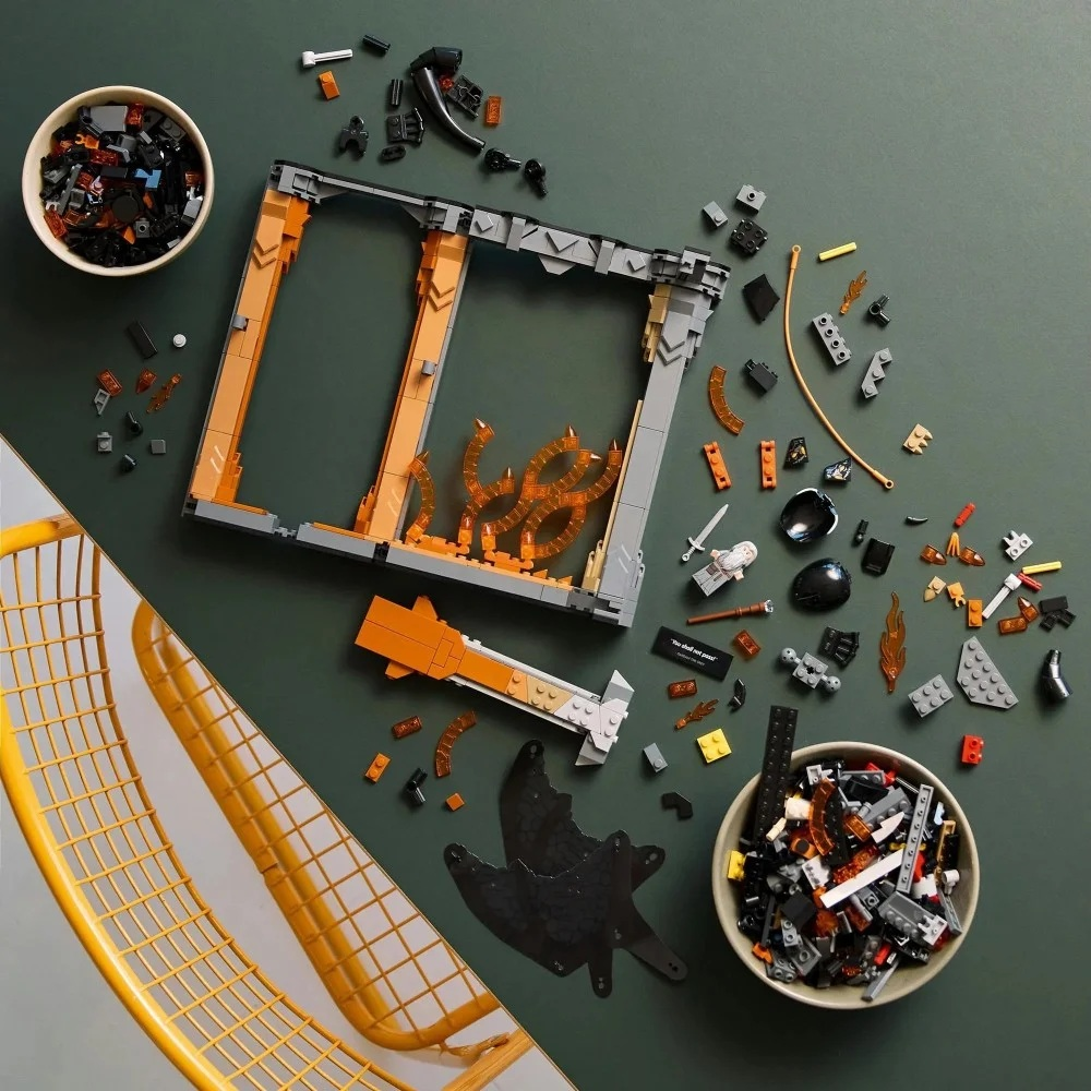 Elementy zestawu Lego są rozrzucone na zielonej powierzchni. Zawiera częściowo zbudowaną konstrukcję, miski z elementami i żółte krzesło.