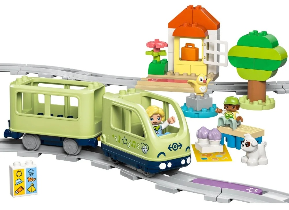 Zestaw pociągu Lego z pociągiem, pasażerami, stacją, drzewem i innymi akcesoriami na torach.