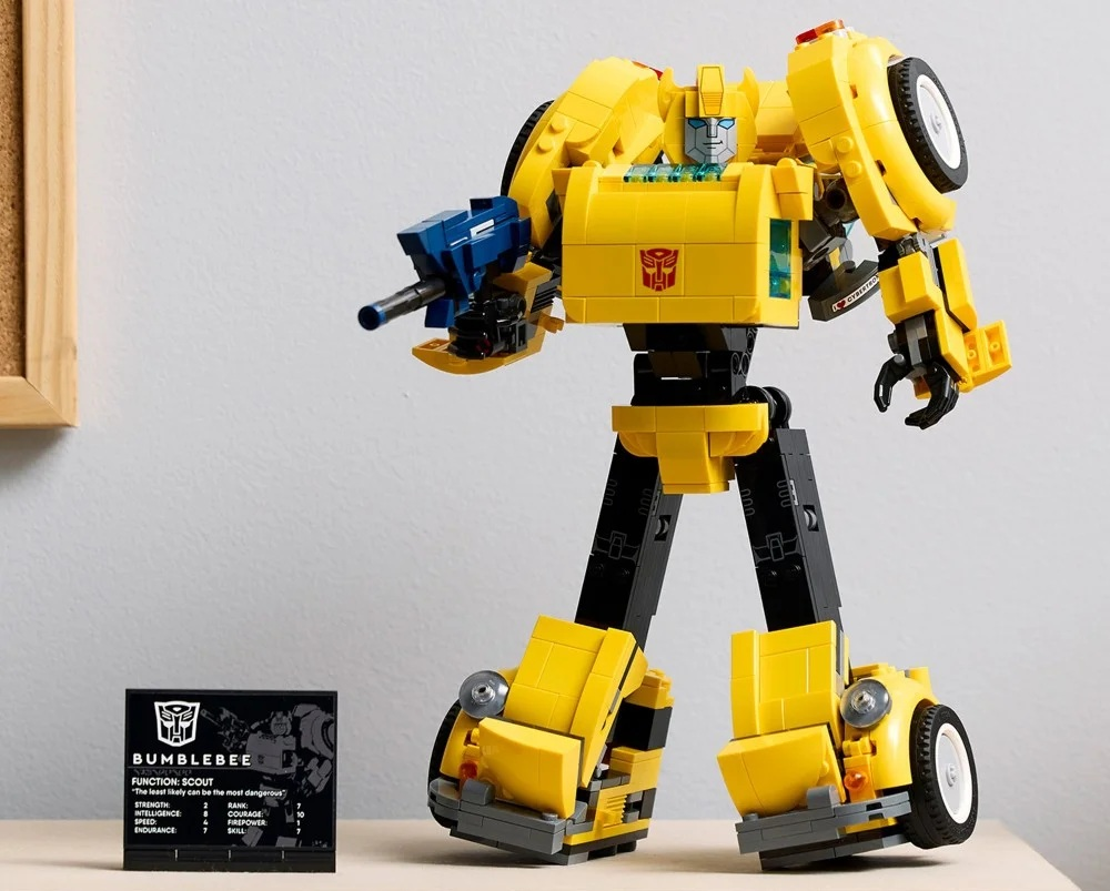 Robot Bumblebee z Lego stoi na stole. Jest głównie żółty z czarnymi nogami i niebieską bronią. Karta wyświetla szczegóły.