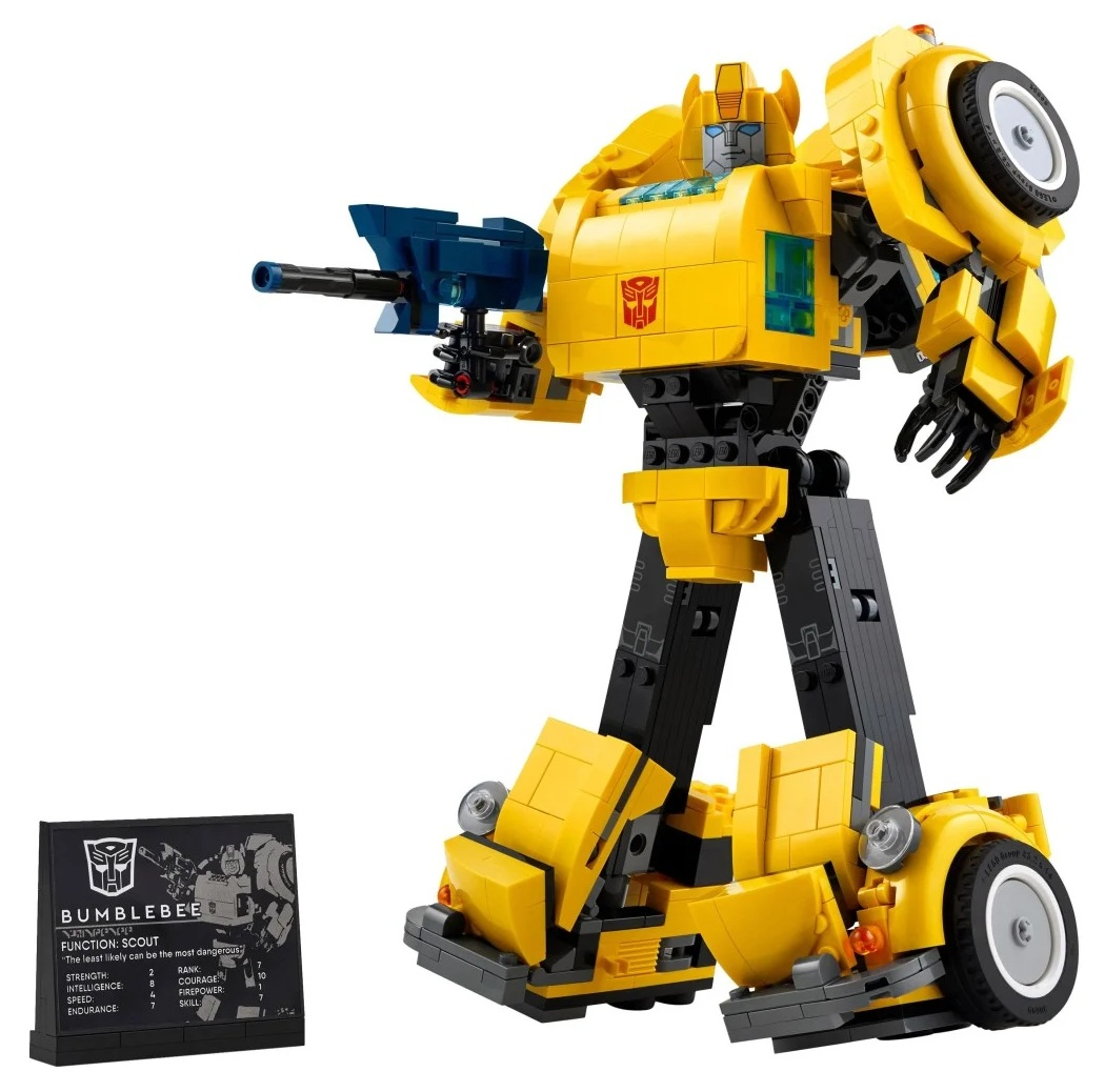 Żółta zabawka Bumblebee Transformer z klocków, trzymająca niebieski pistolet. Czarna karta informacyjna po lewej stronie. Białe tło.