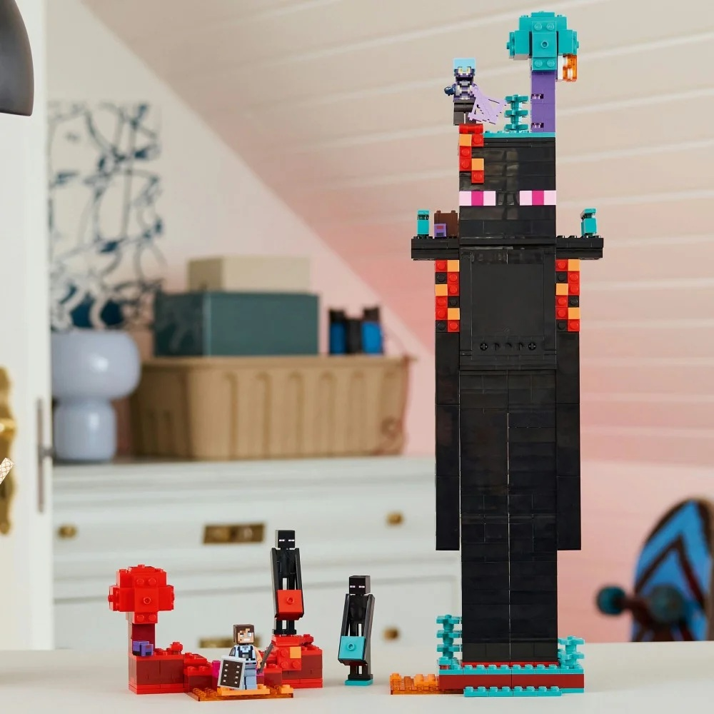 Zestaw Lego Minecraft. Wysoka czarna konstrukcja z figurkami na górze oraz mniejszymi konstrukcjami i figurkami u podstawy.